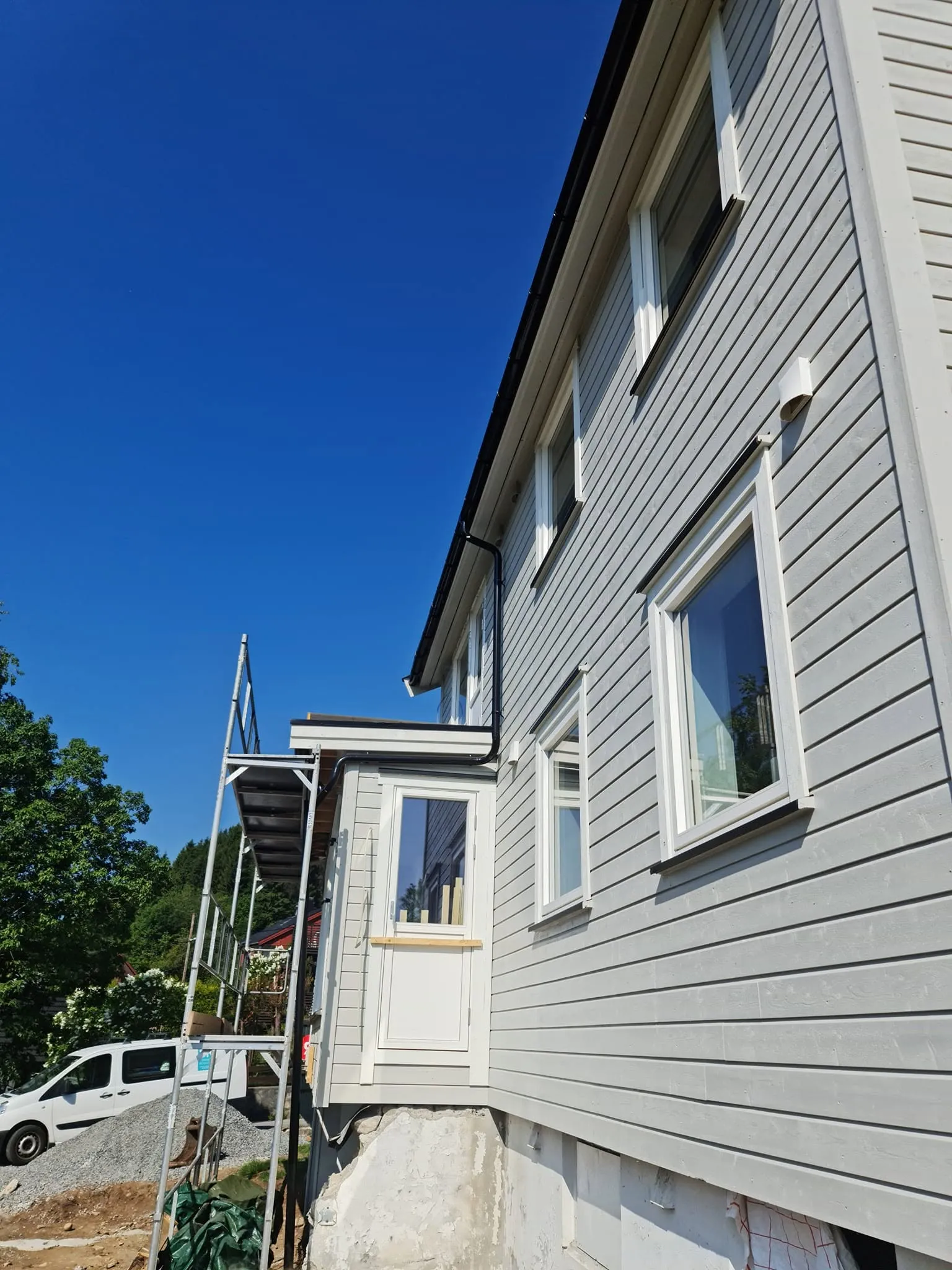 Ferdig fasade med ny kledning, hvite vinduer og svarte nedløp